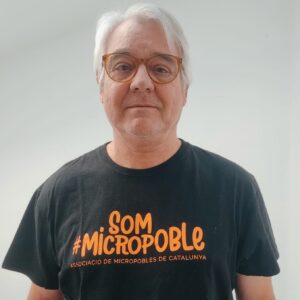 Imatge de Jordi Tarragó, vocal de la Junta de micropobles, dret, somrient a càmara i vestit amb una samarreta que diu "som #micropoble"