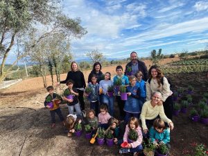 Infants i adults portant testos per a plantar en un espai amb plantes que interessen les abelles